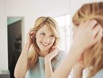 Young woman adjusting hair in mirror, smiling
